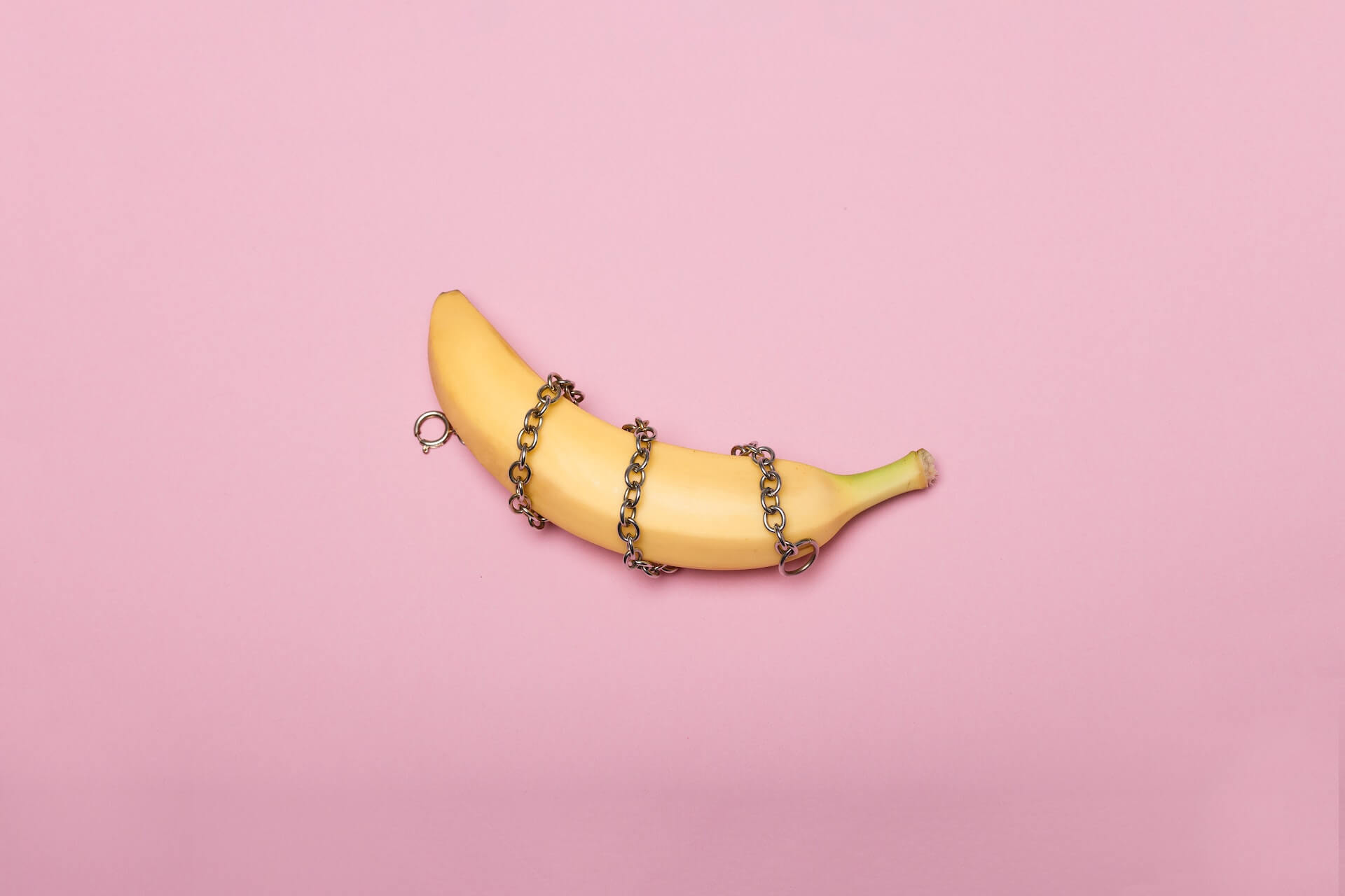 Eine Banane vor rosa Hintergrund mit schwarzer Kette umwickelt