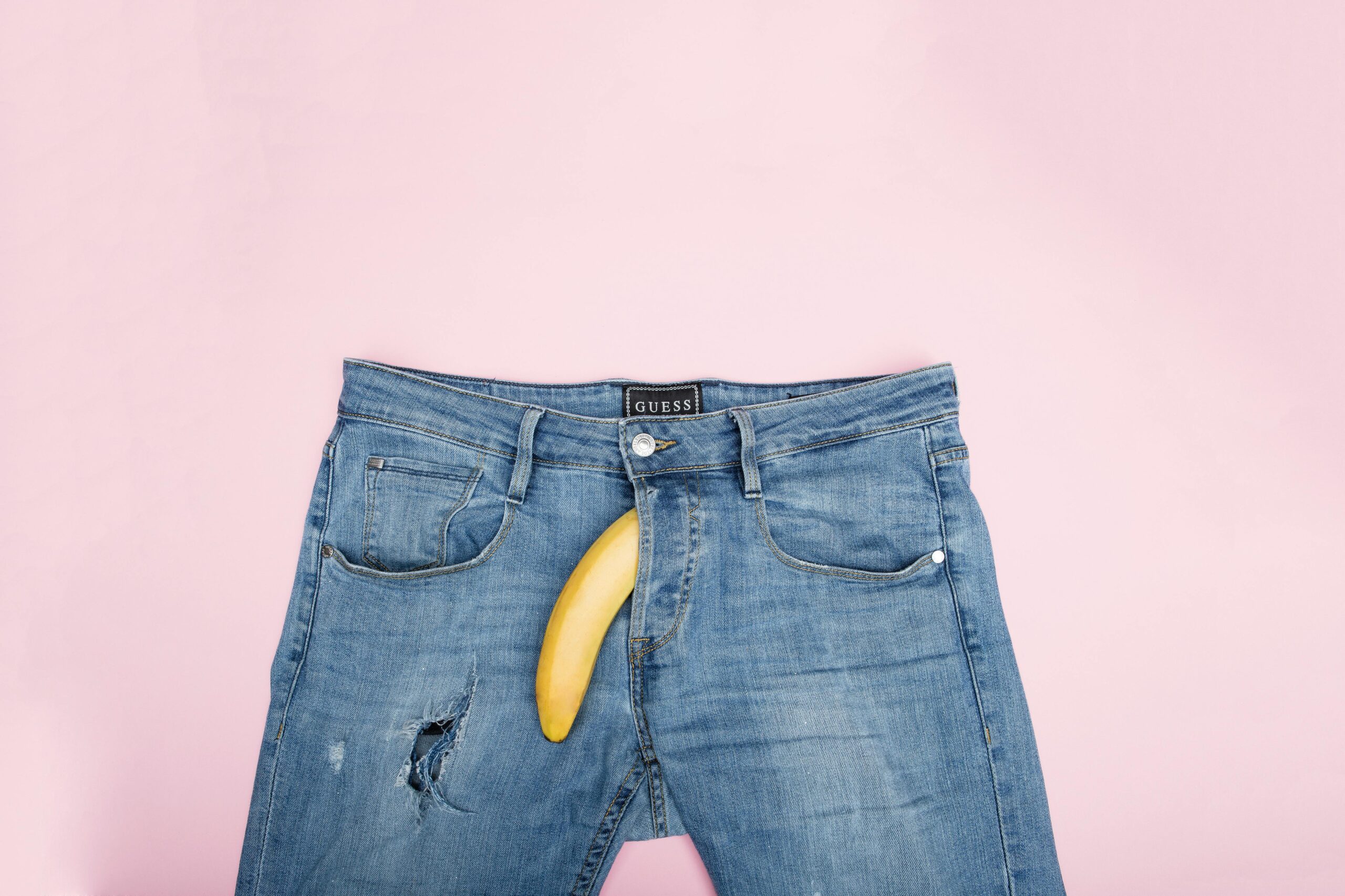 Eine Jenas vor rosa Hintergrund. Aus dem Reißverschluss sieht eine Banane hervor.