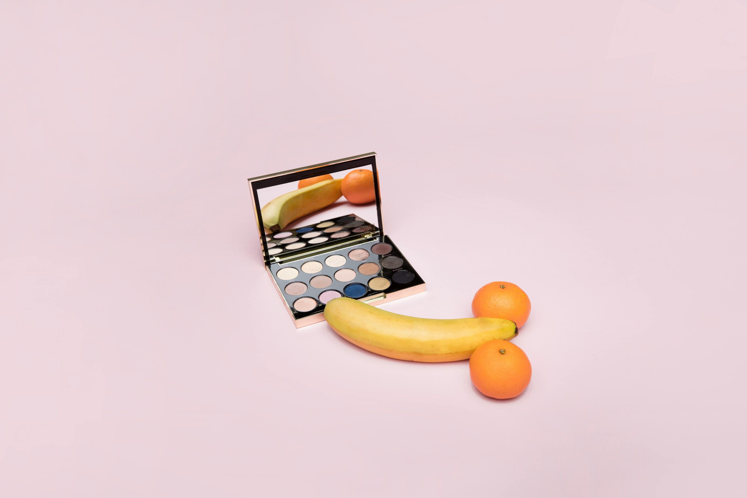 Banane und Mandarinen vor einer Schmink-Schatulle sodass man ihr Spiegelbild sieht.