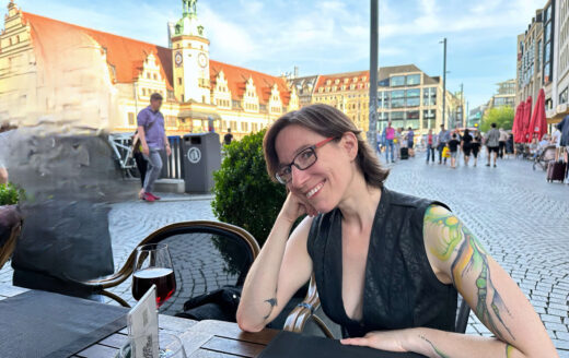 Lächelnde junge Frau mit Tattoos an einem Tisch vor dem Leipziger Marktplatz
