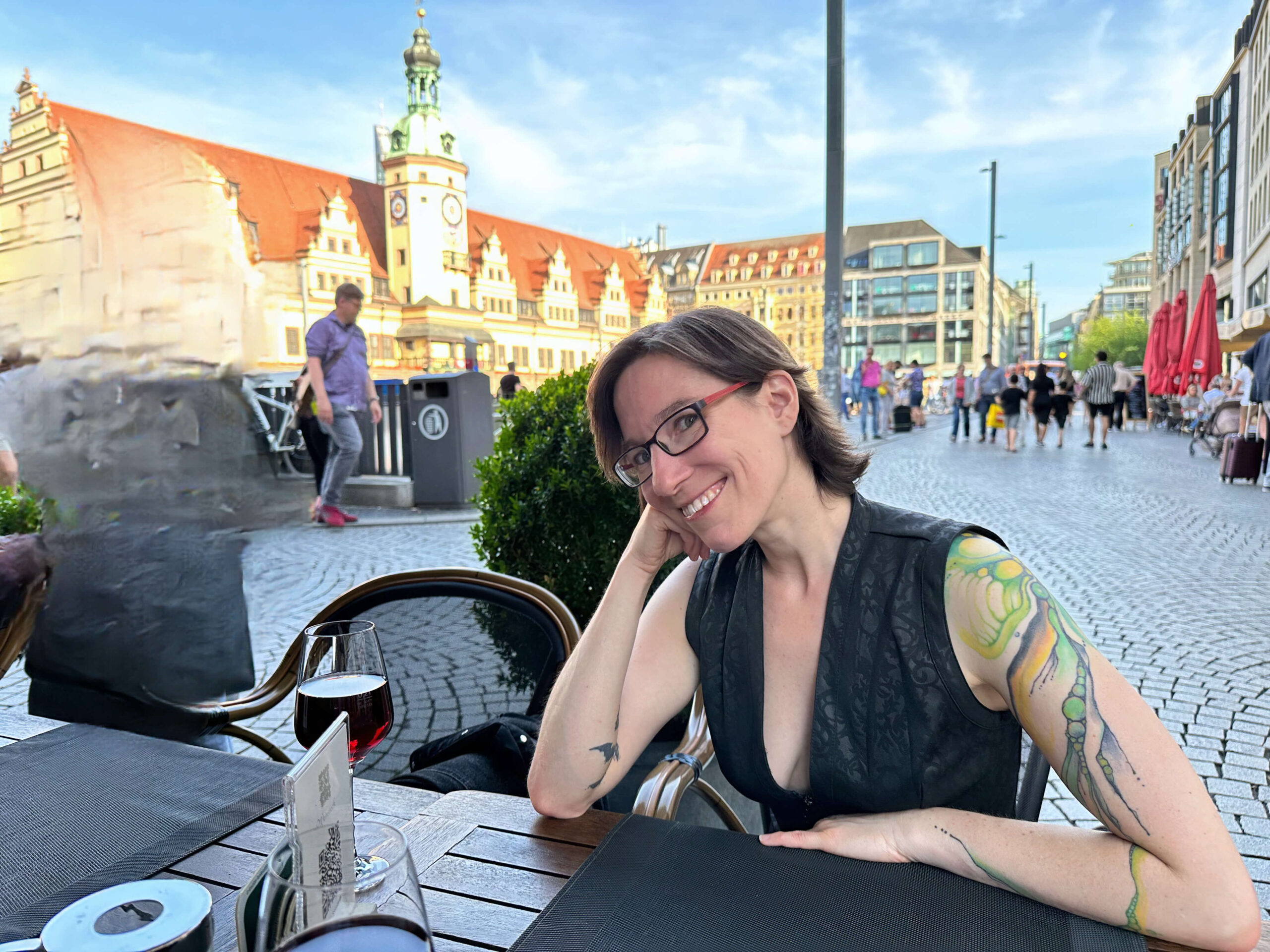 Lächelnde junge Frau mit Tattoos an einem Tisch vor dem Leipziger Marktplatz