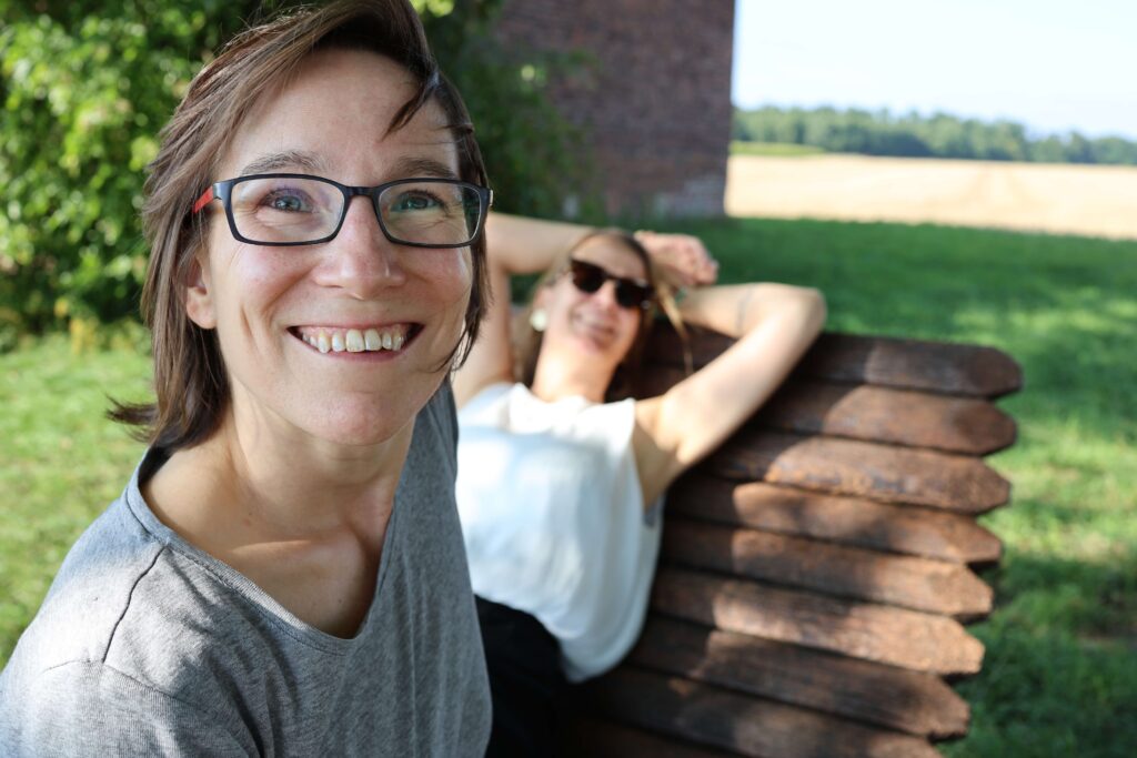 Jay lächelnd im Vordergrund während Tanja von Supportive Sexwork auf der Bank chillt