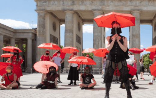 Anonyme Sexarbeitende mit roten Regenschirmen vor dem Brandenburger Tor – Sexarbeitsaktivismus