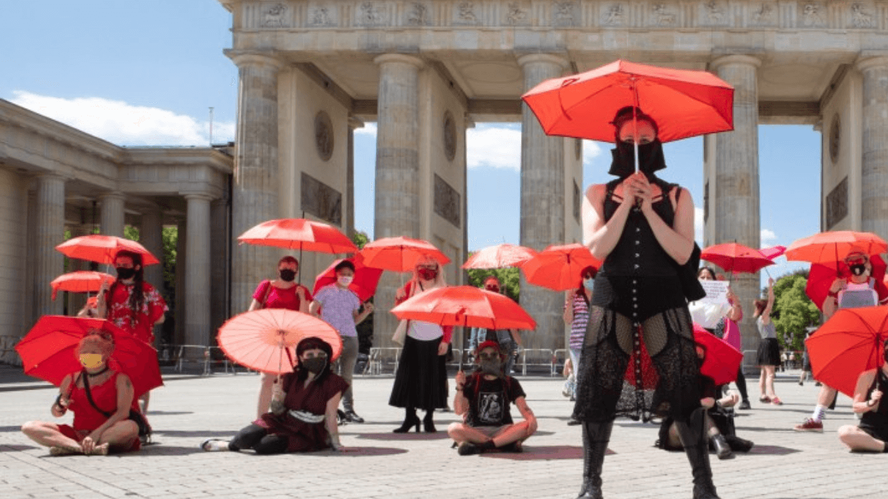 Anonyme Sexarbeitende mit roten Regenschirmen vor dem Brandenburger Tor – Sexarbeitsaktivismus