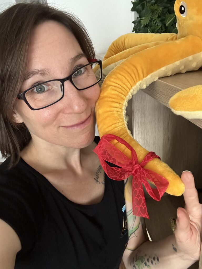 Selfie von Jay, Gesicht am Arm eines Plüsch-Oktopusses mit roter Schleife.