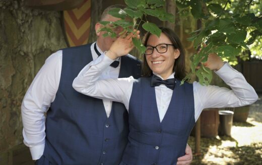 Jay und Sir Chris im Hochzeitsanzug mit Sir Chris hinter Blättern